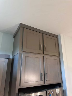 Close-up of stacked painted shaker upper cabinets above the refrigerator